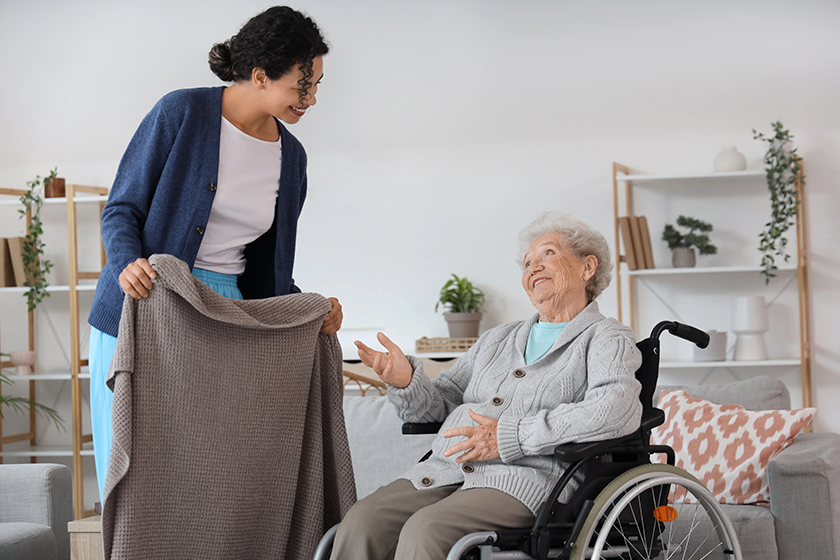 Care associate handing a senior woman in a wheelchair a blanket